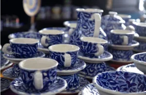 En México Travel Channel nos fascina descubrir las historias que existen detrás de las grandes tradiciones de nuestro país. Hoy entramos a los talleres de Talavera para conocer cómo el barro, los minerales, el fuego y la paciencia dieron vida a una de las expresiones artísticas más reconocibles de México. Talavera de Puebla y Tlaxcala: Una historia de barro, fuego e intercambio cultural La historia de la Talavera mexicana comenzó durante el siglo XVI, cuando alfareros y conocimientos cerámicos procedentes de la península ibérica llegaron a la Nueva España. Sin embargo, el trabajo del barro no era una actividad desconocida en el territorio que hoy ocupa México. Mucho antes de la llegada de los españoles, diversos pueblos mesoamericanos elaboraban vasijas, ollas, comales, incensarios y otros objetos destinados a la cocina, el almacenamiento de alimentos, el transporte de agua y las ceremonias rituales. Los alfareros españoles introdujeron nuevas técnicas relacionadas con los esmaltes vidriados, los pigmentos minerales y los hornos de altas temperaturas. Durante los siglos XVI y XVII, artesanos indígenas, mestizos y españoles comenzaron a combinar conocimientos procedentes de ambos lados del Atlántico. El resultado no fue una copia de los modelos europeos. Fue una tradición nueva. De ese intercambio surgió gradualmente una cerámica con características propias. Los talleres establecidos en Puebla comenzaron a desarrollar formas, decoraciones y procesos que poco a poco distinguieron a la producción local de otras manifestaciones cerámicas de la época. Para el siglo XVII, la Talavera poblana ya había alcanzado prestigio regional y sus piezas circulaban por distintas ciudades de la Nueva España. Durante los siglos posteriores, la tradición continuó evolucionando mediante nuevos diseños, cambios estéticos y adaptaciones técnicas que enriquecieron el oficio sin alterar sus rasgos fundamentales. La UNESCO reconoce que los procesos artesanales practicados actualmente en Puebla, Tlaxcala, Talavera de la Reina y El Puente del Arzobispo conservan elementos esenciales desarrollados desde el siglo XVI y transmitidos de generación en generación. Con el paso del tiempo, la Talavera dejó de ser únicamente un objeto utilitario. Se convirtió en parte del paisaje urbano; cubrió fachadas, templos, patios, fuentes y edificios públicos. Transformó la imagen de Puebla y terminó convirtiéndose en uno de los símbolos visuales más reconocibles de México. La cerámica que cambió la imagen de Puebla Basta caminar por el Centro Histórico de Puebla para comprender la importancia de la Talavera. Las cúpulas cubiertas por azulejos, los patios decorados con mosaicos cerámicos y las fachadas revestidas con patrones geométricos muestran cómo esta tradición terminó formando parte de la arquitectura misma de la ciudad. La Secretaría de Economía y diversas instituciones culturales identifican edificios históricos como la Casa de los Azulejos de la Ciudad de México entre los ejemplos más conocidos del uso monumental de este tipo de cerámica. Durante siglos, la Talavera sirvió para decorar espacios religiosos, residencias privadas y edificios civiles. Pero también permaneció presente en la vida cotidiana a través de platos, jarros, tibores, jarrones y otros objetos domésticos. Sin embargo, la Talavera no fue un producto al alcance de todos. La complejidad de su elaboración, el costo de las materias primas y el trabajo especializado que requería hacían que muchas piezas estuvieran asociadas con conventos, iglesias, edificios públicos, comercios prósperos y familias con suficientes recursos económicos. Mientras amplios sectores de la población utilizaban cerámica común para las actividades cotidianas, la Talavera ocupaba un lugar especial dentro de los hogares acomodados y los espacios de prestigio. Poseer vajillas, azulejos o recipientes decorados con esta técnica también podía comunicar posición social, refinamiento y acceso a bienes considerados de calidad superior. Con el paso del tiempo, la producción se diversificó y hoy es posible encontrar piezas de distintos tamaños, usos y rangos de precio. Sin embargo, la relación entre la Talavera y el trabajo especializado sigue siendo una de las razones que explican su valor. https://twitter.com/SECTUR_mx/status/1470101254777024513 ¿Qué es una Denominación de Origen? La autenticidad de la Talavera no depende únicamente de su diseño. Una Denominación de Origen protege el nombre de productos cuyas características están vinculadas con una región geográfica específica y con los conocimientos desarrollados históricamente por sus comunidades. De acuerdo con el Instituto Mexicano de la Propiedad Industrial (IMPI), esta figura reconoce la relación entre el producto, el territorio, las materias primas y los saberes técnicos que le dan identidad. Por ello, una pieza puede estar inspirada en la Talavera y aun así no ser Talavera protegida. Si fue producida fuera de la región autorizada o no cumple las especificaciones establecidas por la normativa correspondiente, no puede utilizar legalmente esa denominación. ¿Dónde puede producirse legalmente la auténtica Talavera? La auténtica Talavera sólo puede producirse dentro del territorio protegido por la Denominación de Origen. Actualmente dicho territorio comprende: Puebla Distrito Judicial de Puebla Distrito Judicial de Cholula Distrito Judicial de Atlixco Distrito Judicial de Tecali de Herrera Tlaxcala Municipio de San Pablo del Monte La delimitación territorial fue establecida mediante la declaratoria de Denominación de Origen y sus modificaciones posteriores, publicadas en el Diario Oficial de la Federación. Fuera de esta región puede producirse excelente mayólica, loza vidriada o cerámica inspirada en la tradición poblana. Pero no puede utilizar legalmente la denominación protegida. https://twitter.com/SECTUR_mx/status/1417508529783508994 UNESCO y Denominación de Origen: dos reconocimientos distintos Uno de los errores más frecuentes consiste en pensar que la UNESCO certifica piezas de Talavera. En realidad, su reconocimiento está dirigido a los procesos artesanales, la transmisión generacional del conocimiento, las comunidades portadoras de la tradición y los saberes asociados al oficio. La Denominación de Origen, en cambio, regula el uso legal y comercial del nombre Talavera. Por ello, una pieza no adquiere automáticamente la categoría de Talavera protegida por aparecer vinculada a este reconocimiento internacional. El proceso artesanal detrás de una pieza de Talavera La elaboración de una pieza auténtica puede requerir varias semanas. Todo comienza con la preparación de las arcillas, que se limpian, mezclan y amasan para obtener una pasta homogénea libre de impurezas y burbujas de aire. Después, la pieza adquiere forma mediante torno o moldes y pasa por una primera cocción conocida como jagüete, que transforma el barro crudo en una estructura resistente. Posteriormente se aplica el tradicional esmalte blanco opaco elaborado con compuestos de estaño y plomo. Sobre esa superficie aún sin cocer, los decoradores pintan a mano los diseños utilizando pinceles y pigmentos minerales. Finalmente, la pieza regresa al horno para una segunda cocción en la que el esmalte se vitrifica, los colores se fijan y aparece el brillo característico de la Talavera. ¿Cuáles son los colores tradicionales de la Talavera? La documentación técnica vinculada con la Denominación de Origen reconoce tradicionalmente seis colores principales: Azul Amarillo Negro Verde Naranja Malva El blanco corresponde al fondo generado por el esmalte opaco. Aunque el azul es el color más emblemático, históricamente la Talavera desarrolló una paleta más amplia reconocida por la tradición artesanal. El craquelado: Cuando el esmalte deja ver su historia Algunas piezas presentan una fina red de líneas superficiales conocida como craquelado. Este efecto aparece debido a la diferencia de comportamiento entre la cubierta vítrea y el cuerpo cerámico durante el enfriamiento. No se trata necesariamente de una falla. En numerosas piezas tradicionales forma parte de la apariencia normal del esmalte. Sin embargo, el craquelado por sí solo no demuestra autenticidad. Para determinar si una pieza está protegida por la Denominación de Origen es necesario revisar también su procedencia y certificación. ¿Cómo identificar una pieza de Talavera auténtica? La mejor forma consiste en verificar la información del productor. Antes de comprar conviene revisar: Nombre del taller autorizado. Información de identificación del fabricante. Marcado correspondiente en la base de la pieza. Datos de certificación aplicables. Comprobante de compra que identifique claramente al establecimiento. También es recomendable adquirir las piezas directamente en talleres reconocidos o distribuidores autorizados. La autenticidad de la Talavera no depende únicamente de su apariencia visual, sino de su origen documentado. Comprar directamente a talleres reconocidos ayuda a proteger el trabajo artesanal y evita la confusión con productos industriales inspirados en la Talavera. San Pablo del Monte: La tradición tlaxcalteca de la Talavera La historia de la Talavera no pertenece exclusivamente a Puebla. Desde la época virreinal, las comunidades alfareras ubicadas en lo que hoy es San Pablo del Monte, Tlaxcala, mantuvieron una estrecha relación con los talleres poblanos. La cercanía geográfica facilitó el intercambio de materias primas, conocimientos técnicos, mano de obra especializada y rutas comerciales vinculadas a la producción cerámica. Con el paso de los siglos, esta tradición artesanal se consolidó también en territorio tlaxcalteca, formando parte del mismo entorno cultural que dio origen a la Talavera novohispana. Por ello, cuando se delimitó legalmente la Denominación de Origen, se reconoció que la historia, los saberes y los procesos de San Pablo del Monte estaban profundamente vinculados con los de Puebla. Actualmente, el municipio forma parte del territorio protegido por la Denominación de Origen Talavera y participa, junto con Puebla, en la conservación de una tradición artesanal que ha perdurado durante más de cuatro siglos. Hablar hoy de Talavera implica reconocer el trabajo de las comunidades artesanas de ambos estados, cuya experiencia y conocimientos continúan dando forma a una de las expresiones cerámicas más importantes de México. Un oficio que sigue transmitiéndose de generación en generación La UNESCO destaca que el conocimiento continúa transmitiéndose principalmente dentro de talleres y familias. Algunos artesanos dominan el proceso completo, otros se especializan en etapas específicas: Preparación del barro. Torneado. Decoración. Esmaltado. Manejo del horno. Cada pieza terminada es resultado de un trabajo colectivo acumulado durante años de aprendizaje. Por eso el valor de la Talavera no se encuentra únicamente en el objeto final. También reside en el conocimiento necesario para producirlo. ¿Cuánto cuesta una pieza auténtica de Talavera? El precio de una pieza auténtica depende de factores como el tamaño, la complejidad del diseño, el número de colores utilizados y las horas de trabajo requeridas para su elaboración. En talleres certificados pueden encontrarse pequeñas piezas utilitarias, como tazas, salseras o platos, con precios que suelen comenzar en varios cientos de pesos. Las piezas medianas decoradas a mano pueden alcanzar varios miles de pesos, mientras que tibores, lavabos, murales y trabajos arquitectónicos elaborados por encargo pueden superar ampliamente esas cantidades. Buena parte del costo no corresponde únicamente a la materia prima. También refleja semanas de trabajo artesanal, múltiples procesos de cocción, la intervención de diferentes especialistas y la conservación de conocimientos transmitidos durante generaciones. Por ello, adquirir una pieza auténtica de Talavera implica comprar un objeto funcional o decorativo, pero también apoyar un oficio reconocido tanto por la Denominación de Origen como por la UNESCO. La auténtica Talavera no nace solamente del barro Una pieza puede tener flores azules, fondo blanco y un craquelado atractivo, pero eso no basta para convertirla en Talavera. La auténtica Talavera nace de una combinación única de territorio, materias primas, conocimiento artesanal, regulación técnica y transmisión generacional. Su historia comienza en el barro; continúa en las manos de torneros, pintores y horneros y termina en piezas que conservan las huellas visibles del trabajo humano. Por eso, cuando observamos un plato, un azulejo o un tibor auténtico, no estamos viendo únicamente cerámica, vemos más de cuatro siglos de conocimiento, territorio y trabajo artesanal convertidos en arte. ¿Te gustaría conocer más sobre esta y otras tradiciones que hacen único a México? Visita nuestro sitio web México Travel Channel y síguenos en nuestras redes sociales para descubrir los destinos, la cultura y las historias que enriquecen nuestro país./Foto: Sectur